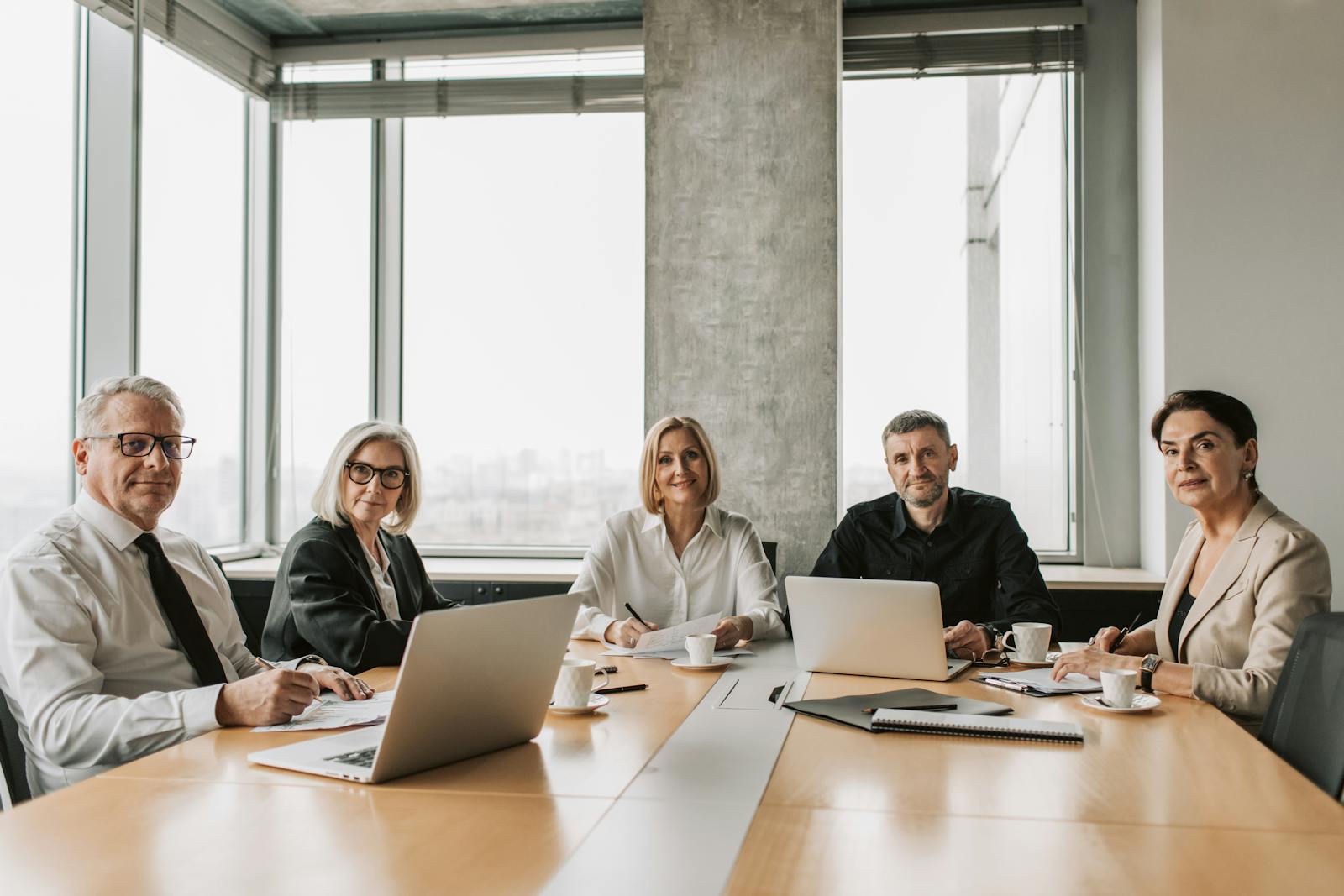 A team of mature business professionals in a meeting around a conference table with laptops and documents.