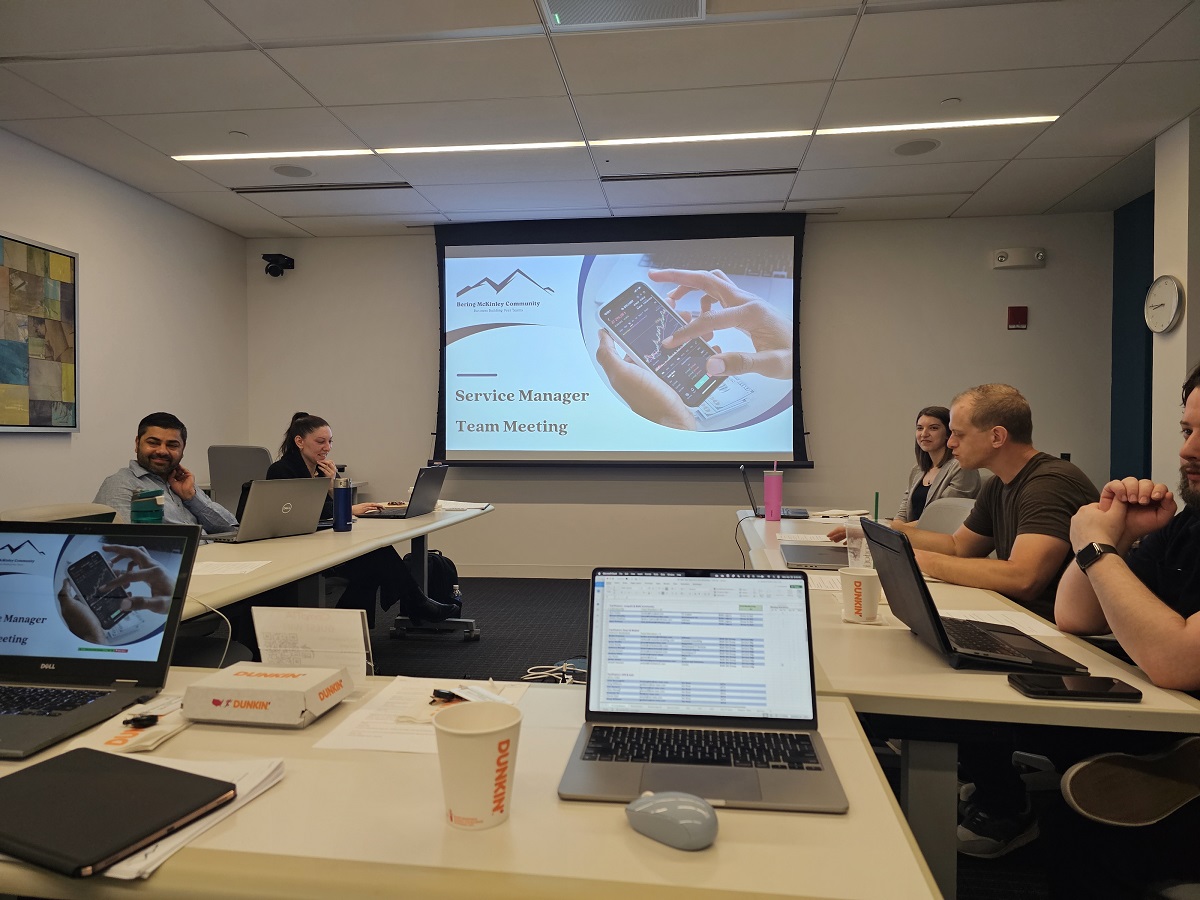 A team meeting in a modern conference room with a presentation on "Service Manager Team Meeting" displayed on the projector screen.